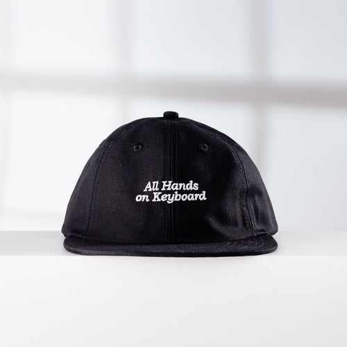 Black cap with 'All Hands on Keyboard' text on a white surface with a light gray background