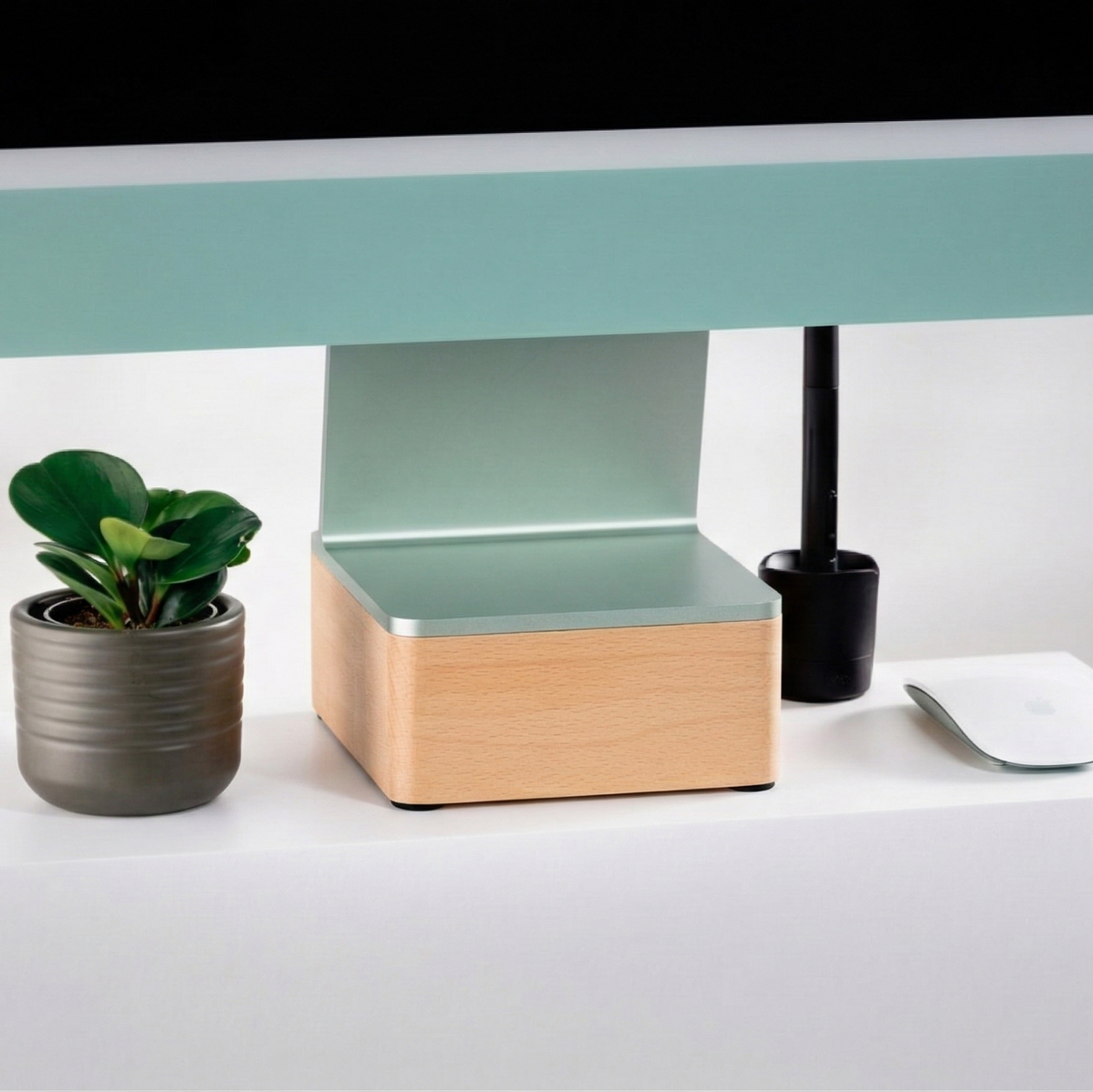 Green 24” iMac on top of a solid 24” iMac Riser on a white desk with a plant