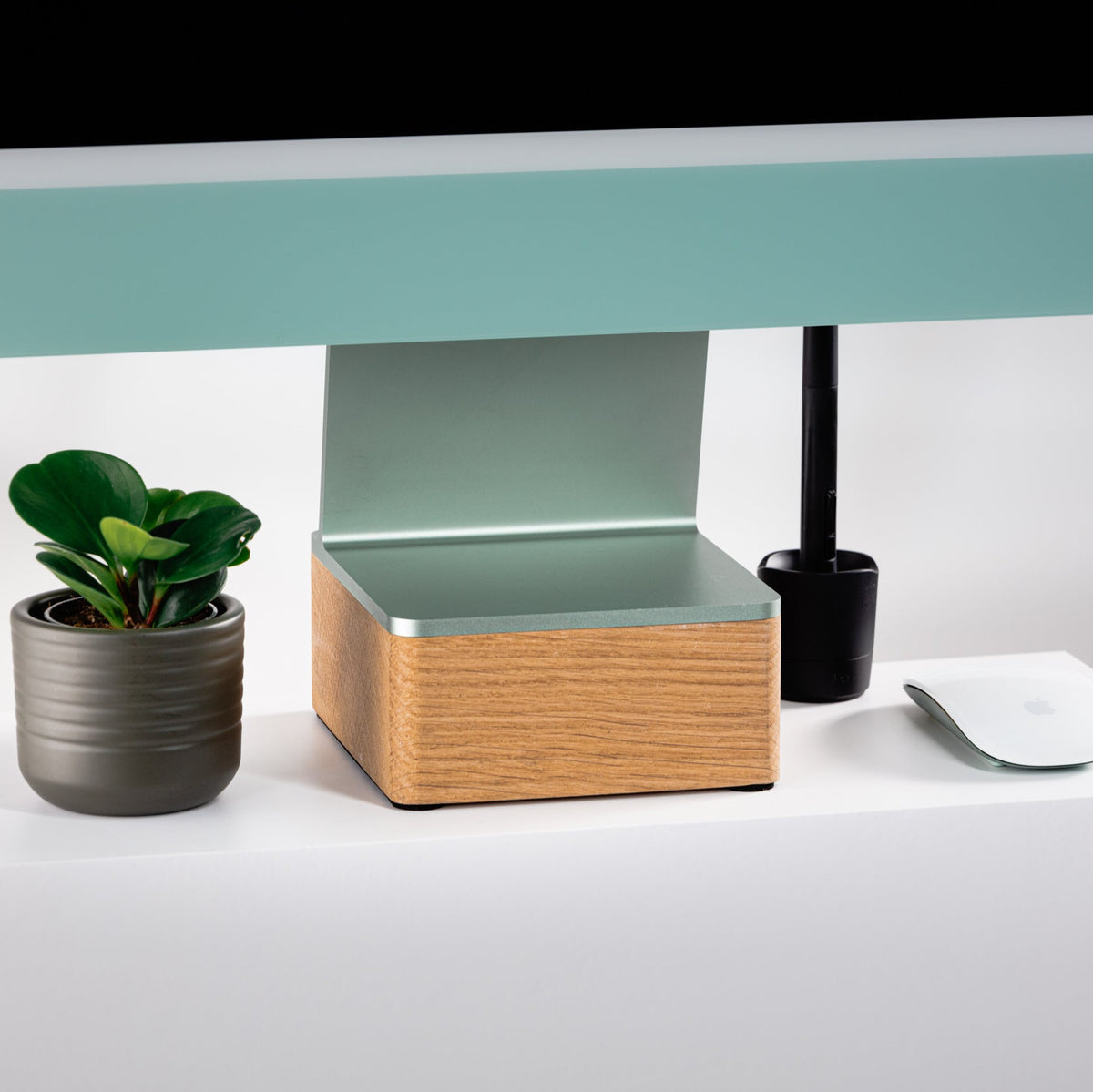 Modern office setup with a green 24” iMac on top of a solid 24” iMac Riser and plant on a white surface